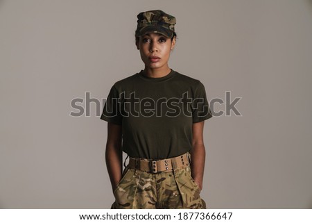 Confident african american soldier woman posing with hands in her pockets isolated over grey wall