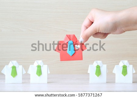 Leadership and teamwork concept, Woman hand holding origami shirt with tie and leading among small yellow shirt on wooder background