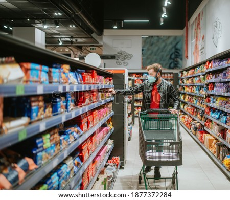 Photo of a man in a leather jacket and jeans, wearing a medical protective mask and buying in a supermarket.