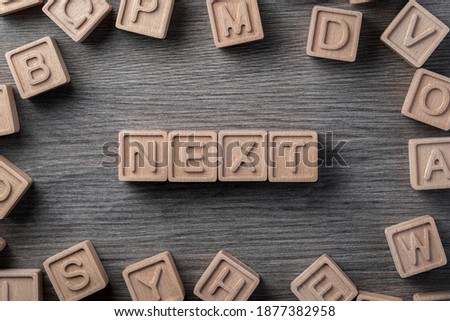 the word "next" is made up of square wooden cubes with letters on a wooden gray surface