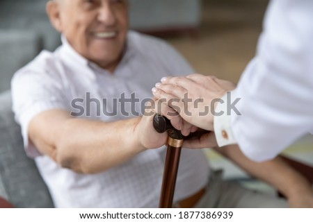 Close up of nurse caregiver palms covering hand of smiling senior patient holding cane. Sick old man struggle with trauma consequence make success on rehabilitation therapy with help support of doctor Royalty-Free Stock Photo #1877386939