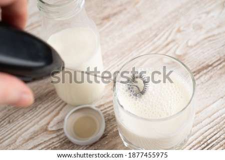 Mixing milk in glass by milk frother. Making foamy milk with frother. Milk handheld mixer. Royalty-Free Stock Photo #1877455975