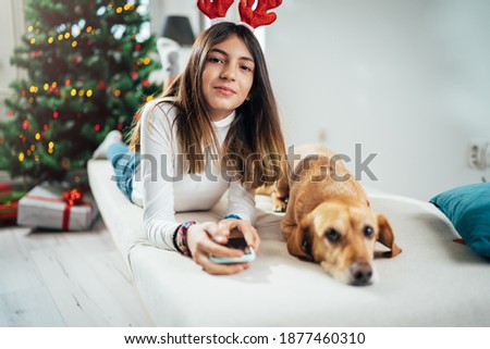 A girl with deer antlers posing with a dog by the Christmas tree