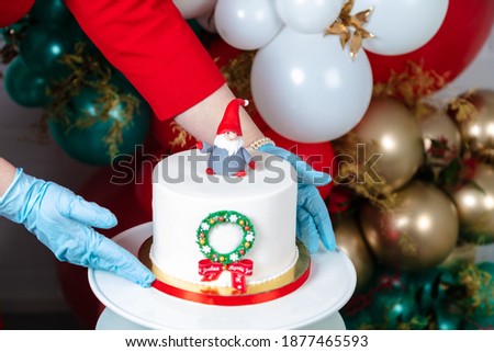 Spreading the Christmas cake onto a plate, a gloved hand cropped the photo. Happy Christmas lettering.
  Happy holiday concept