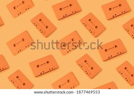 Pattern made with retro audio cassettes on modern orange background. Creative concept of retro technology. 70's or 80's aesthetic. Flat lay, top view.