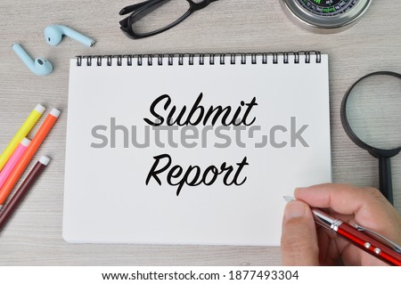 Selective focus of pen colors, earphone, eyeglasses, compass, magnifying glass and man hand holding pen writing with text SUBMIT REPORT. Business and education concept.