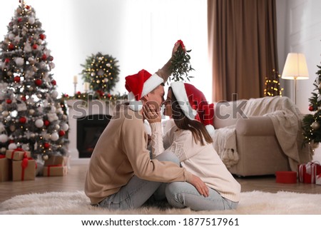 Couple kissing under mistletoe in room decorated for Christmas