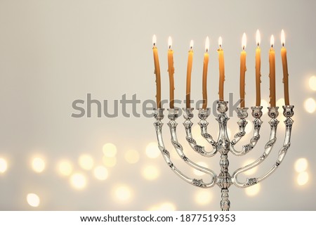 Silver menorah with burning candles against light grey background and blurred festive lights, space for text. Hanukkah celebration