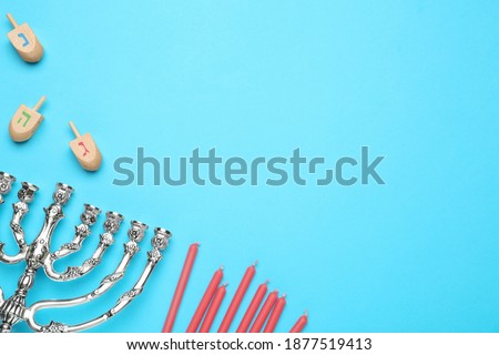 Silver menorah, red candles and Hanukkah dreidels with Nun, He, Gimel symbols on blue background, flat lay. Space for text