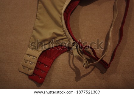 The two red and beige women bras hanging from the brown cushion. 