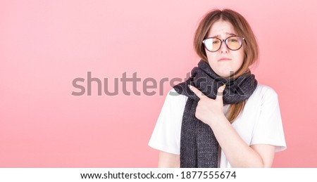 Sick young woman points her finger to the space to her right. Portrait of a ill girl with a scarf around the neck on a pink background.