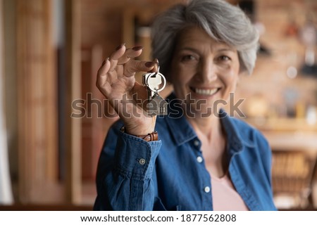 Happy old middle aged sincere beautiful hoary woman showing keys in hands, feeling excited of buying apartment or selling successfully dwelling, older people and real estate agency service concept. Royalty-Free Stock Photo #1877562808
