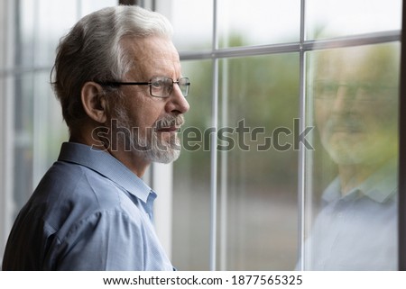 Pensive elderly mature senior man in eyeglasses looking in distance out of window, thinking of personal problems. Lost in thoughts elderly middle aged grandfather suffering from loneliness, copy space Royalty-Free Stock Photo #1877565325