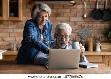 Smiling older mature hoary woman pointing finer at laptop screen, choosing holidays trip with relaxed senior husband online. Happy middle aged family couple using modern tech gadget together at home.