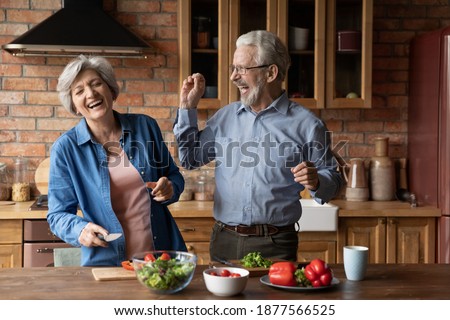 Overjoyed emotional middle aged senior married family couple having fun preparing food together in kitchen, having playful mood. Sincere happy old husband and wife laughing, cooking meal at home. Royalty-Free Stock Photo #1877566525