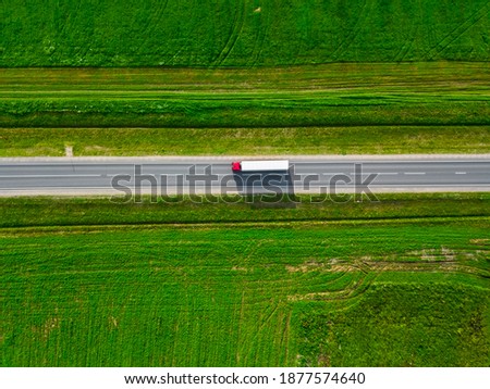 Top view aerial shot of a beautiful landscape with a truck moving on a road between green fields