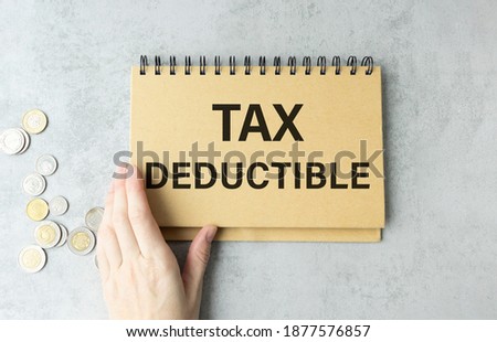 Closeup on businessman holding a card with text TAX DEDUCTIBLE, business concept image with soft focus background and vintage tone