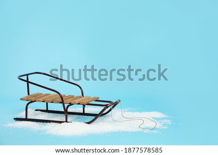 Stylish sleigh in pile of snow on light blue background, space for text