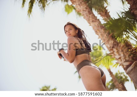 cute young teenage girl or woman posing and having fun on the beach under palm trees in summer swimsuit . Trendy girl posing. Funny and positive woman in sunglasses