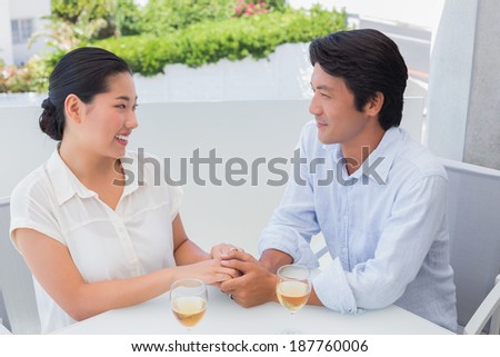 Happy couple holding hands and having white wine outside on a balcony