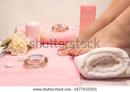 The picture of ideal done pedicure. Female legs in the spa spot in the white background. Composition of white and pink shower accessories and towels.