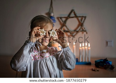 Family celebrating Hanukkah. Father lighting candles on traditional menorah and giving a gift to his daughter. Crafted Star of David with dry branches on the wall, Jewish holiday, lifestyle