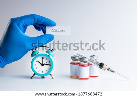 medical vaccine vials with red liquid and alarm clock over gray background. time to vaccination concept. vaccine requirement conceptual.