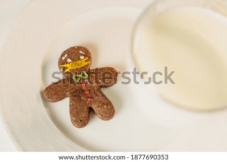 covid-19 themed cookies. a cookie that looks like someone wearing a protective mask. Gingerbread wearing a medical mask. a cookie and a glass of milk on a coffee table. Stay home, keep social distance