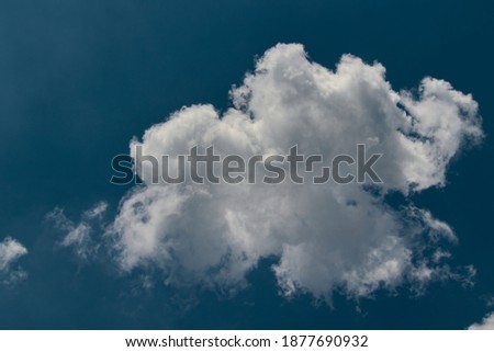 white cumulus cloud illuminated by the sun, floating calmly under a slightly misty blue sky.