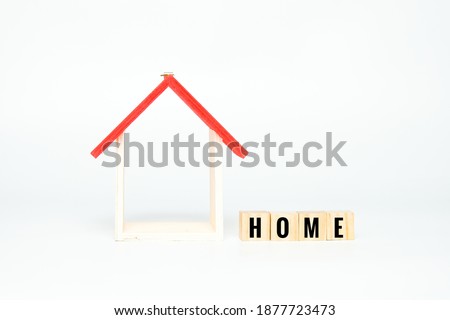 A picture of house frame miniature with a wooden block written HOME on white background.