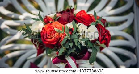 Bright flower arrangement of red and white roses on light blurry background, close-up. Wedding bouquet of fresh flowers with green twigs and satin ribbons.