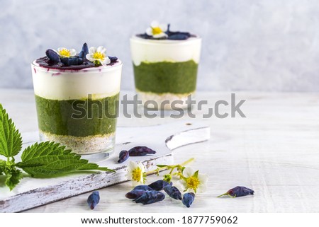 Delicious dessert with a layer of yogurt, smoothie with nettle, oat flakes and honeysuckle. Dessert served in a glass with a spoon.