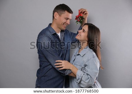 Happy couple standing under mistletoe bunch on grey background