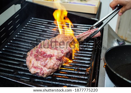 Beef.Tomahawk rib beef steak on hot black grill with flames