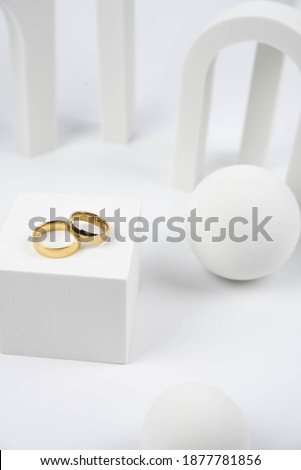 Golden wedding rings on trendy white podium. Aesthetic still life art photography.