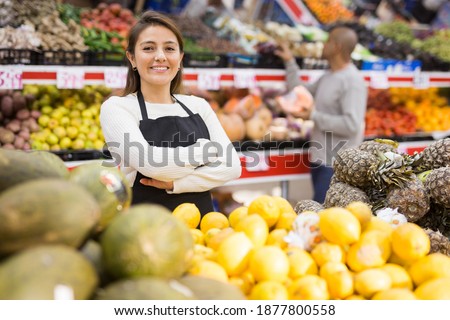 Supermarket woman worker in black apron putting melons in his department Royalty-Free Stock Photo #1877800558