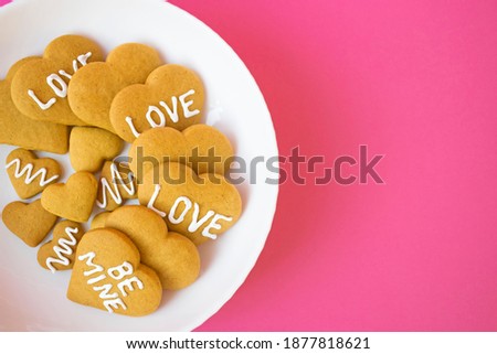 Plate with handmade butter cookies in heart shape with frosting and words of love on pink background. Valentines Day treat, homemade bakery as gift or treat for teatime. Copy space.