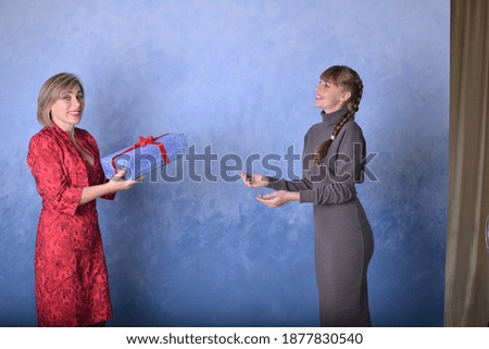 Mom and daughter give and throw a gift on a blue background. Happy family, adult daughter. Concept of the holiday, new year, christmas, sale, promotion.