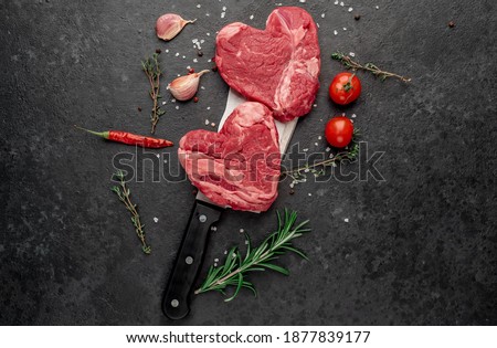 Two raw marbled beef steak in the shape of a heart on a meat knife with spices on a stone background