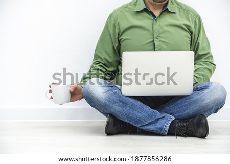Cropped picture of successful businessman sitting on the floor with white laptop and cup of coffee, involved in working process.