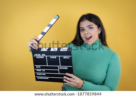Young caucasian woman over isolated yellow background holding clapperboard very happy having fun