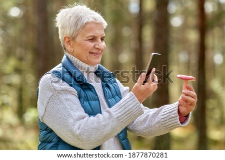 technology, people and leisure concept - senior woman with smartphone using app to identify mushroom in forest