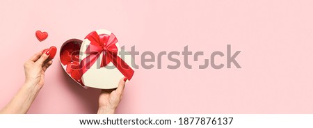 Woman hands holding red hearts from Valentine's Day gift box on pink background. Romantic greeting card with copy space. View from above.