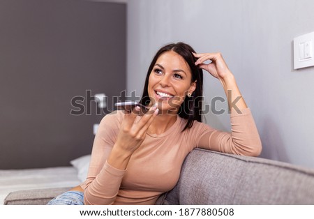 Smiling beautiful woman talking on the phone at home, happy young girl holds cellphone making answering call, attractive girl having pleasant conversation chatting by mobile with friend