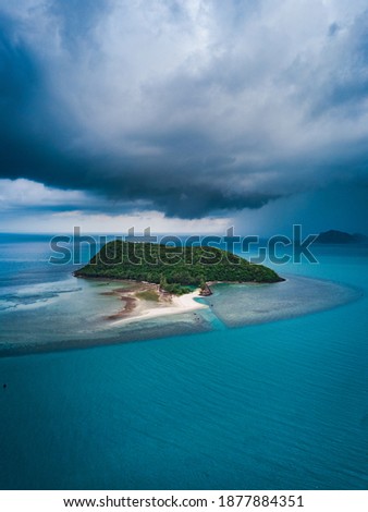 Top view aerial shot of a beautiful landscape with a small tropical island and a rainstorm coming from behind