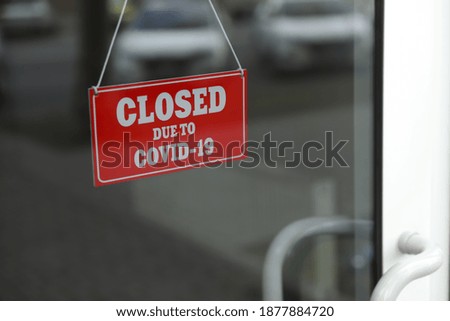 Red sign with words "Closed Due To Covid-19" hanging on glass door