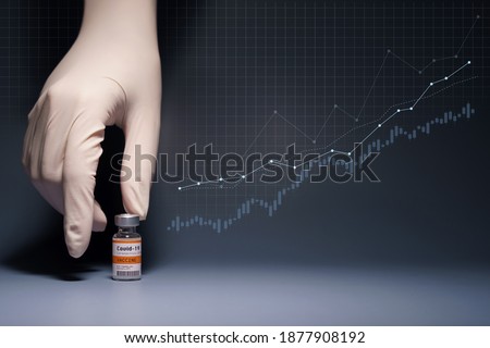 Global economy recovery after Covid 19 Vaccination success concept. Hands of a researcher in medical gloves pick up a Coronavirus Vaccine vial with stock index chart rising up in the background. Royalty-Free Stock Photo #1877908192