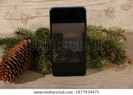 Smartphone with working screen and modern frameless design, vertically on a wooden background with fir branches and pine cone. Working smartphone on the screen of room interior design.