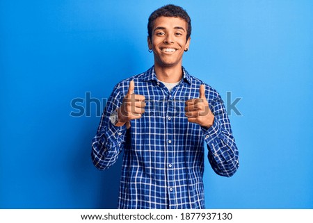 Young african amercian man wearing casual clothes success sign doing positive gesture with hand, thumbs up smiling and happy. cheerful expression and winner gesture. 