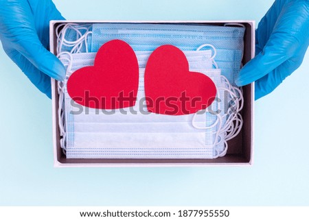 Hands in blue medical gloves hold an open gift box with protective medical masks and two red heart shapes. Safe gifts concept. Actual gift for Valentine's Day during the coronavirus period